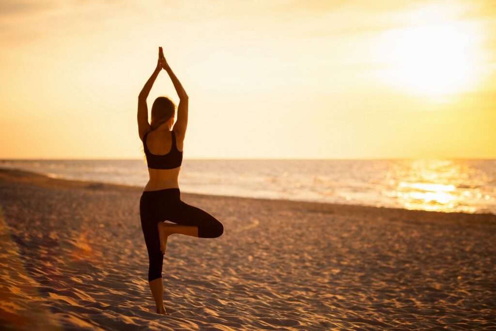 Woman practicing yoga on beach at sunset.