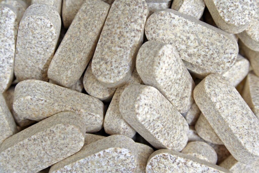 Pile of textured, beige supplement tablets.