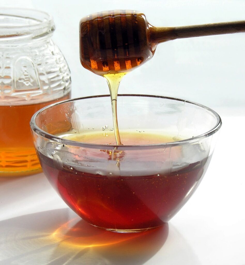 Honey drizzling into a glass bowl.