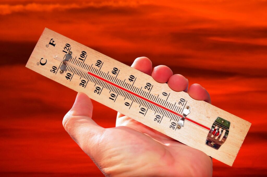 Hand holding thermometer against red sky.