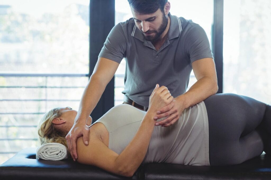 Therapist assisting woman with shoulder exercise.