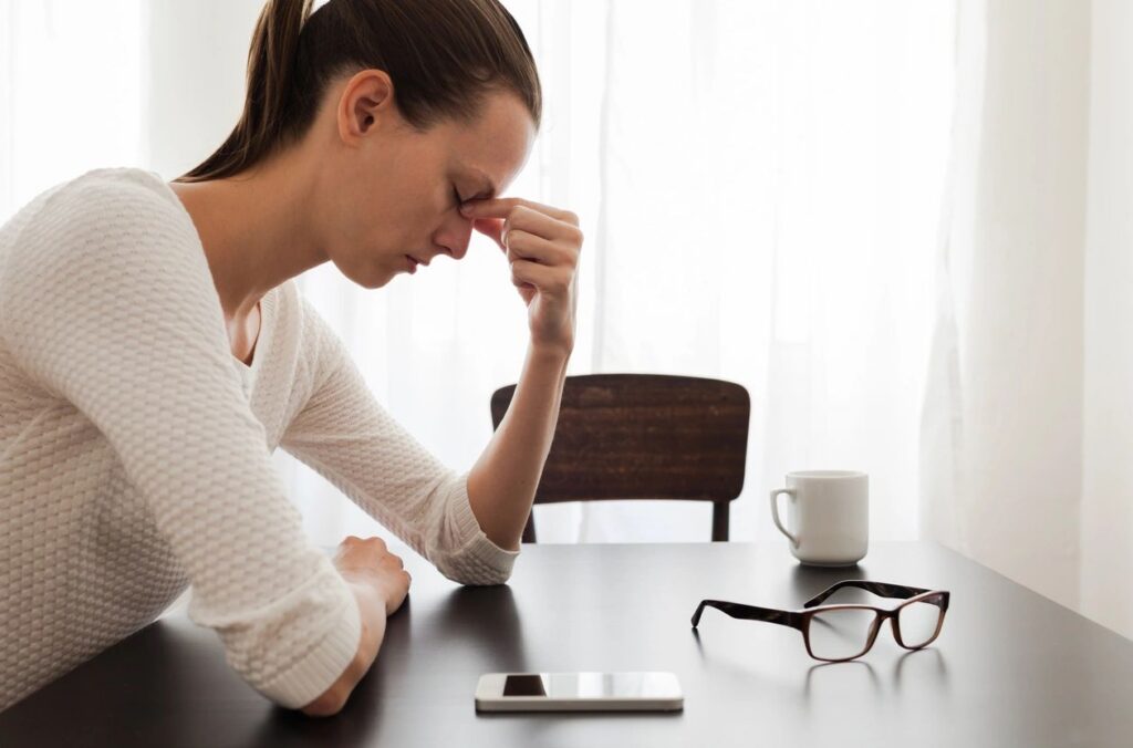 Woman stressed at table with smartphone.