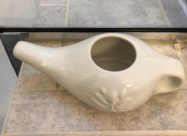 White ceramic neti pot on tiled surface.