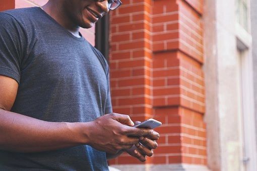 Man texting on smartphone near brick wall.
