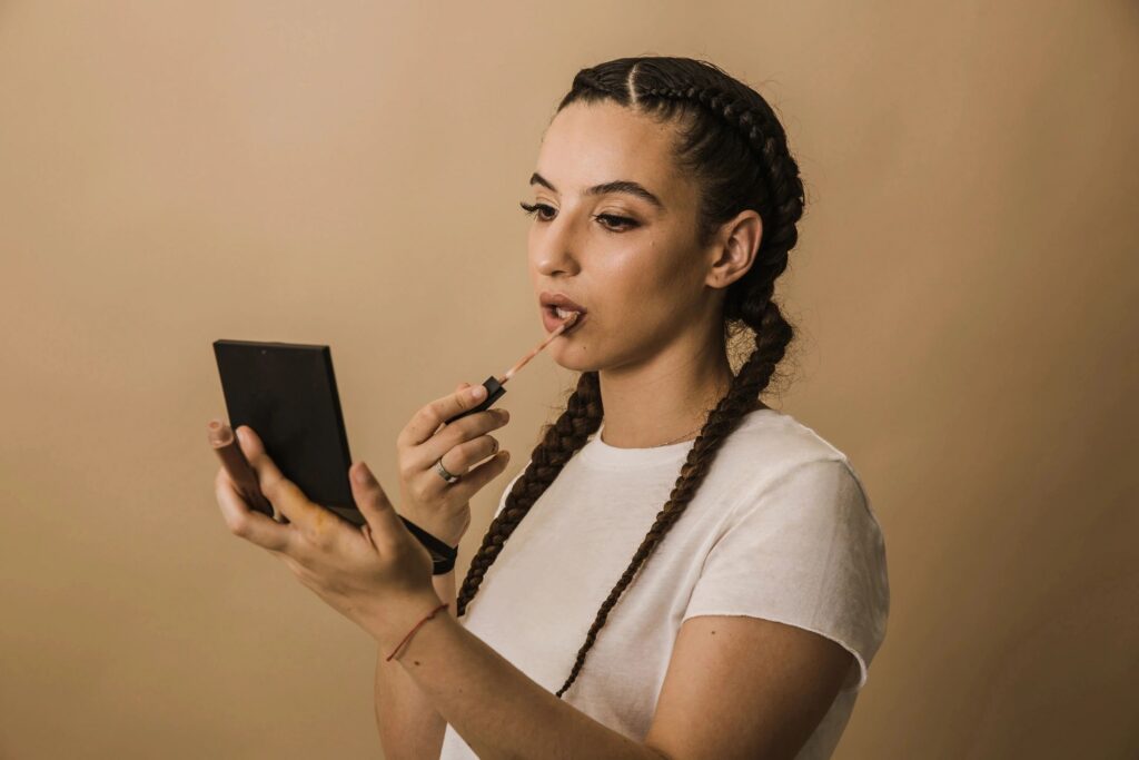 Woman applying lipstick, holding a mirror.