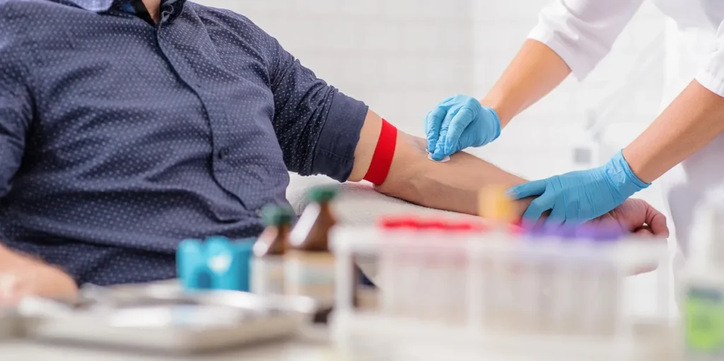 Man sitting at a table with a nurse wearing gloves administering a blood sample to him