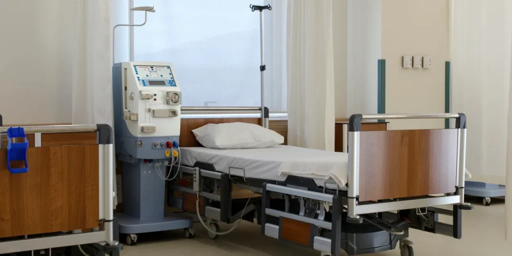 Hospital room with a bed, a monitor, a stand, a cupboard, a trolley, a wall with curtains