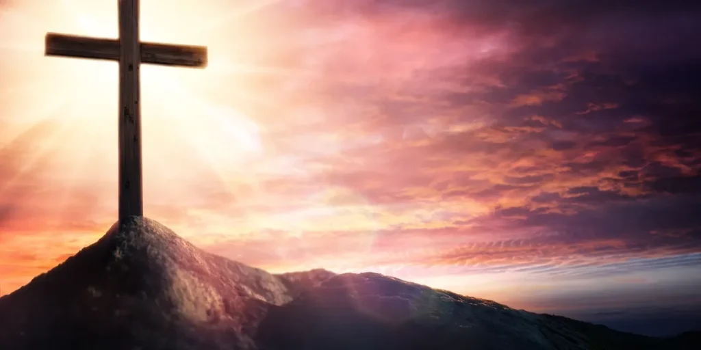Cross atop a mountain with the sun setting in the background, surrounded by clouds in the sky