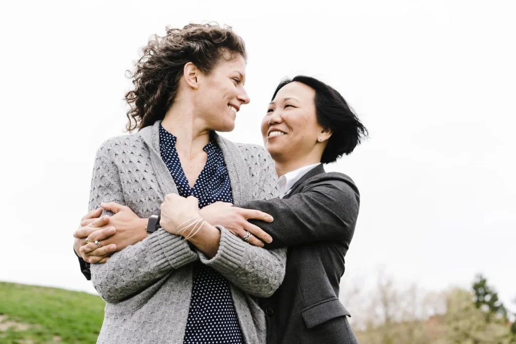 Two women embracing in a field, both of them The woman on the left is wearing a jacket