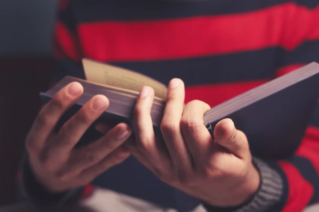 Person wearing a red and t-shirt, holding a book in their hands and reading it intently