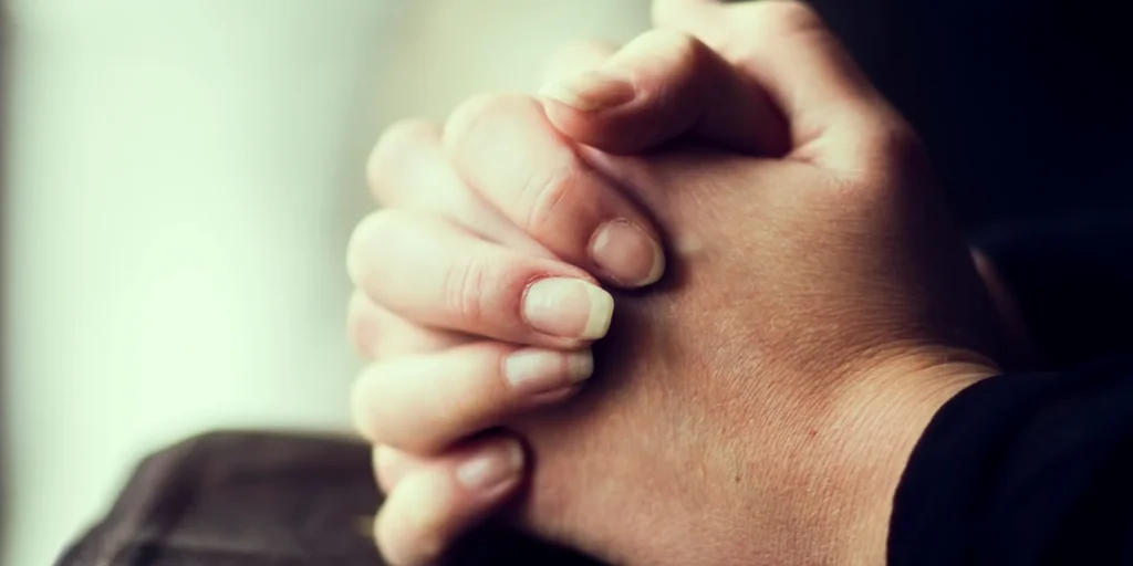 Person with their hands clasped together in prayer, their fingers intertwined in a gesture of reverence and devotion