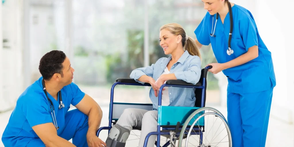 Woman in a wheelchair being assisted by two nurses wearing stethoscopes, with a blurred background