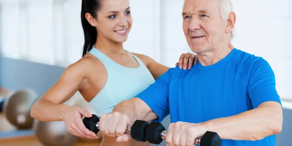 Older man and woman working out with dumbbells in a gym, with a wall in the background