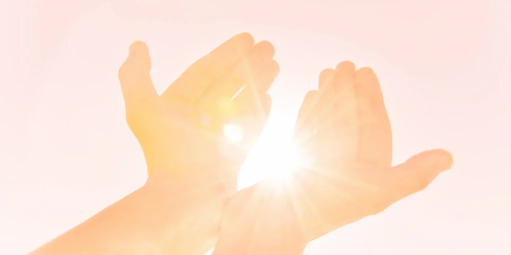 Person with their hands outstretched in the air, illuminated by the sun's rays