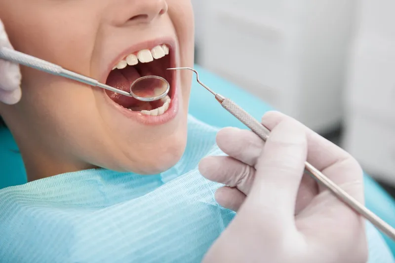 Woman getting her teeth examined by a dentist, with a person holding a dental tool in their hand
