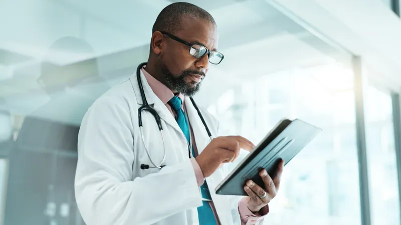 Male doctor wearing a coat and a stethoscope around his neck, holding a tablet computer in his hands