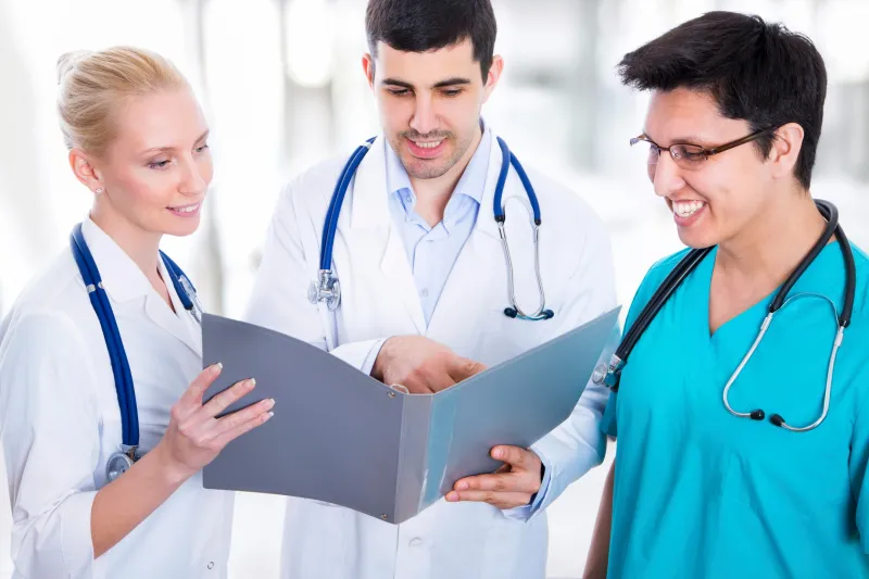 Three doctors wearing stethoscopes and looking at a clipboard, with a blurred background