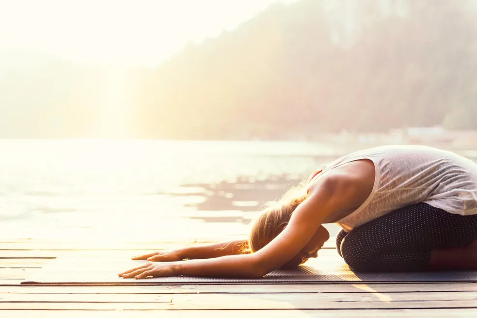 Woman in a yoga pose on a dock at sunset, with a wooden surface beneath her