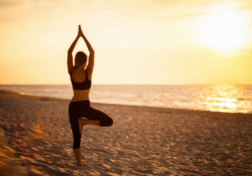 Woman practicing yoga on beach at sunset.