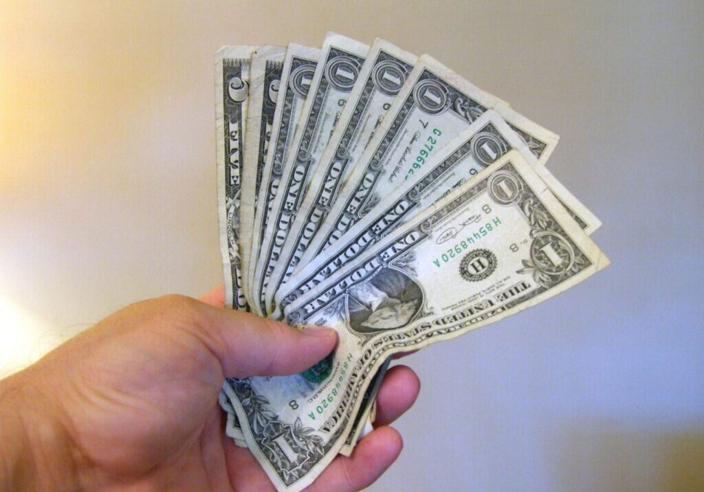 Hand holding several one-dollar bills.