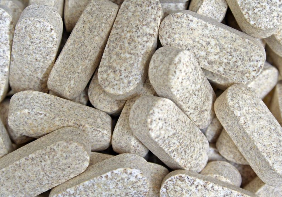 Pile of textured, beige supplement tablets.