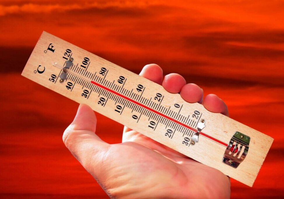 Hand holding thermometer against red sky.