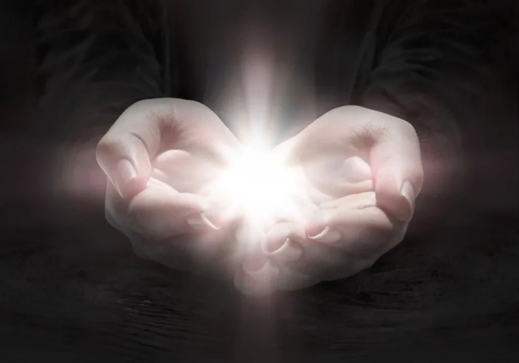 Person holding a light in their hands, illuminated by a bright light emanating from their palms