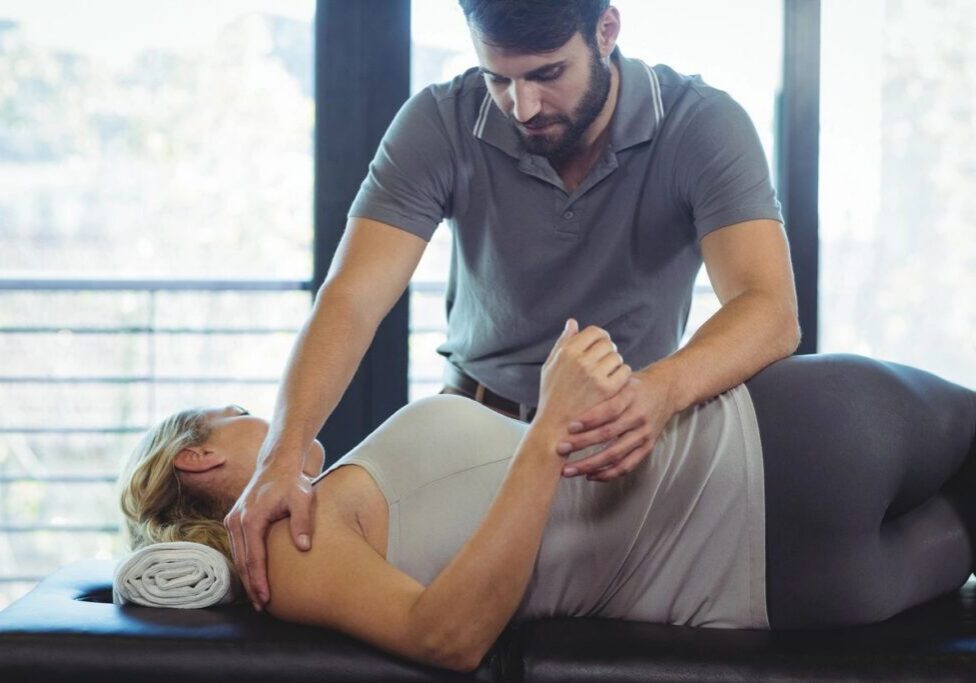 Therapist assisting woman with shoulder exercise.
