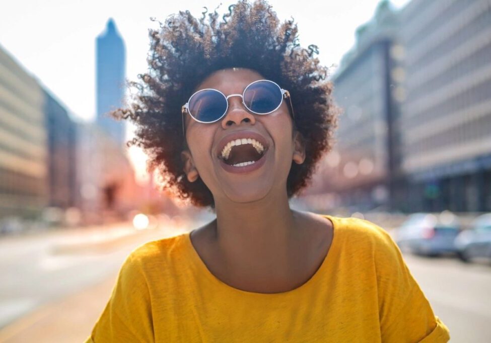 Smiling person wearing sunglasses on city street.