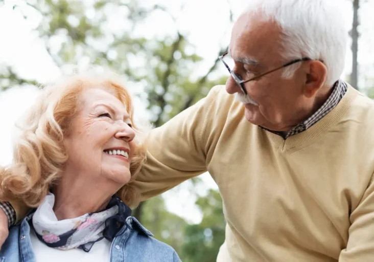 Older couple at each other in the woods, with the man wearing spectacles and the woman wearing a jacket