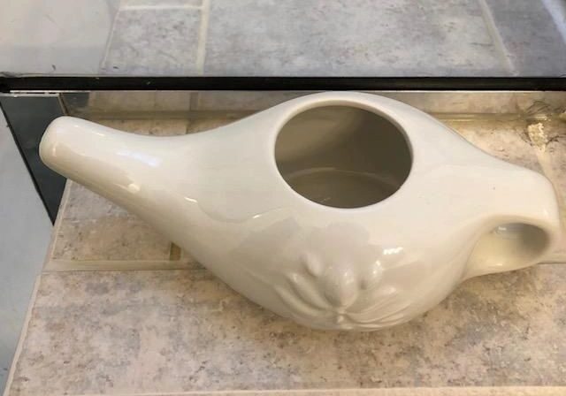 White ceramic neti pot on tiled surface.