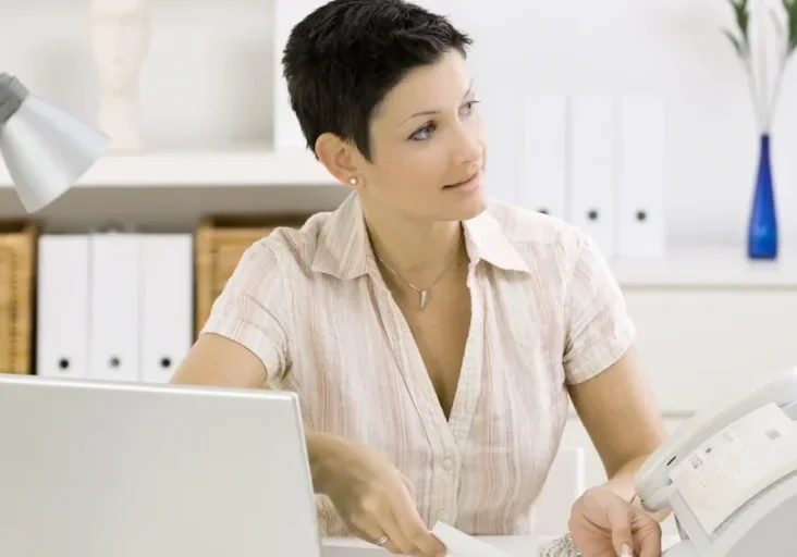 Woman sitting at a desk with a laptop, a printer, a lamp