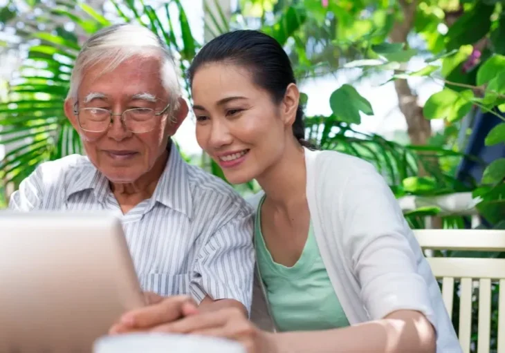 Older man and woman sitting at a table, looking intently at a laptop