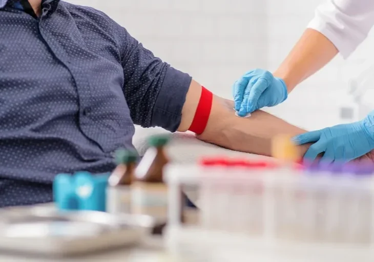Man sitting at a table with a nurse wearing gloves administering a blood sample to him