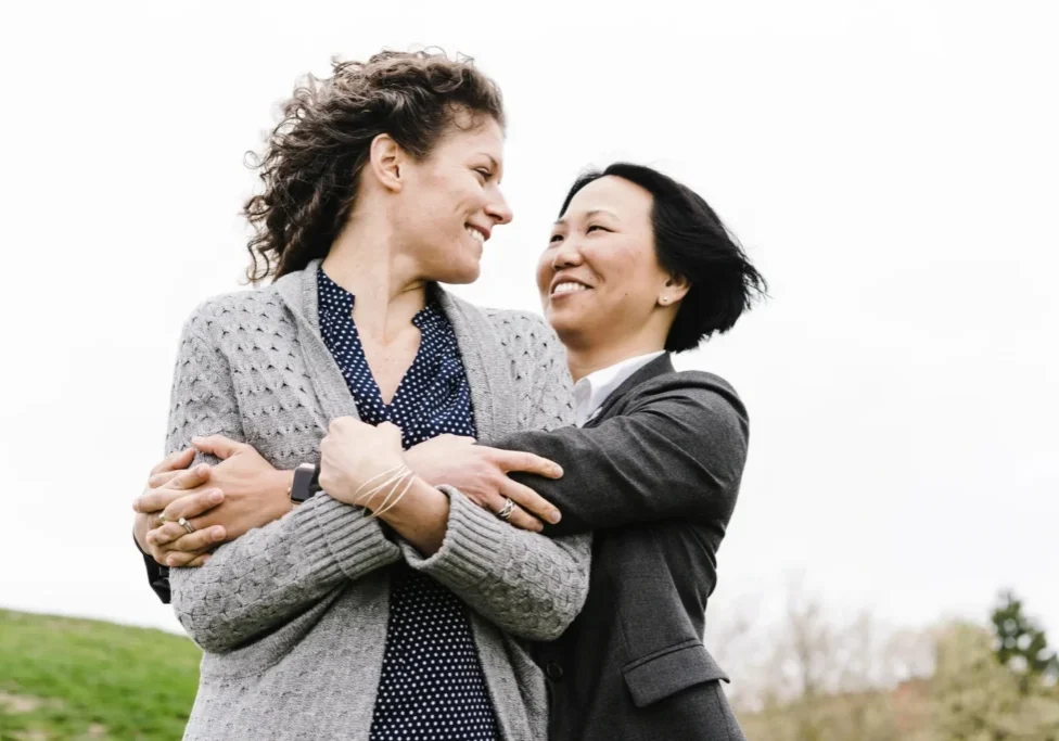 Two women embracing in a field, both of them The woman on the left is wearing a jacket