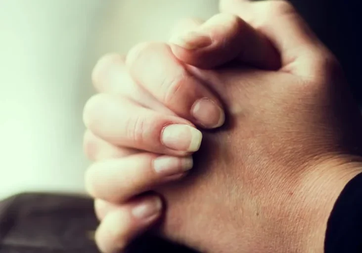 Person with their hands clasped together in prayer, their fingers intertwined in a gesture of reverence and devotion