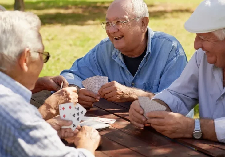 Four older men sitting around a wooden table, playing cards