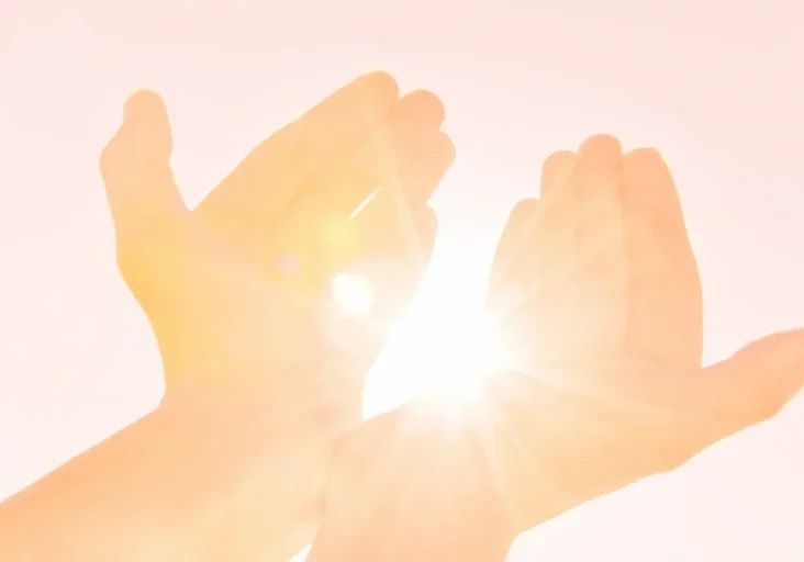 Person with their hands outstretched in the air, illuminated by the sun's rays