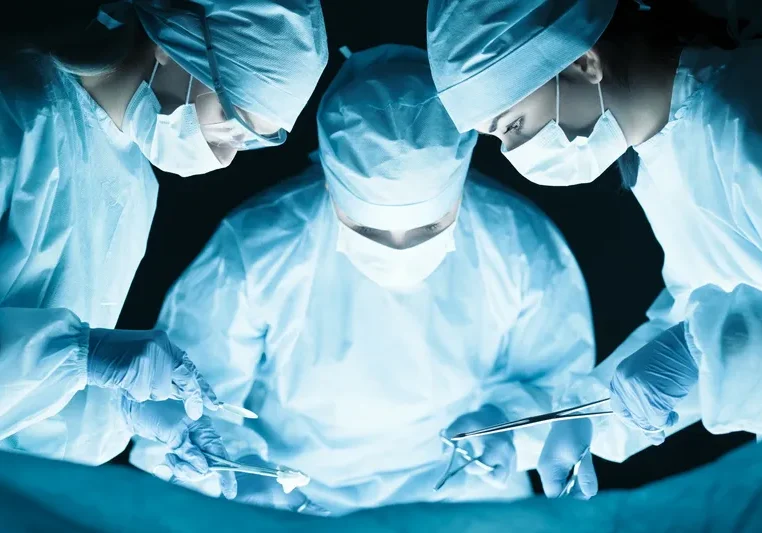 Three surgeons wearing masks, caps, gloves, and coats, performing surgery in an operating room