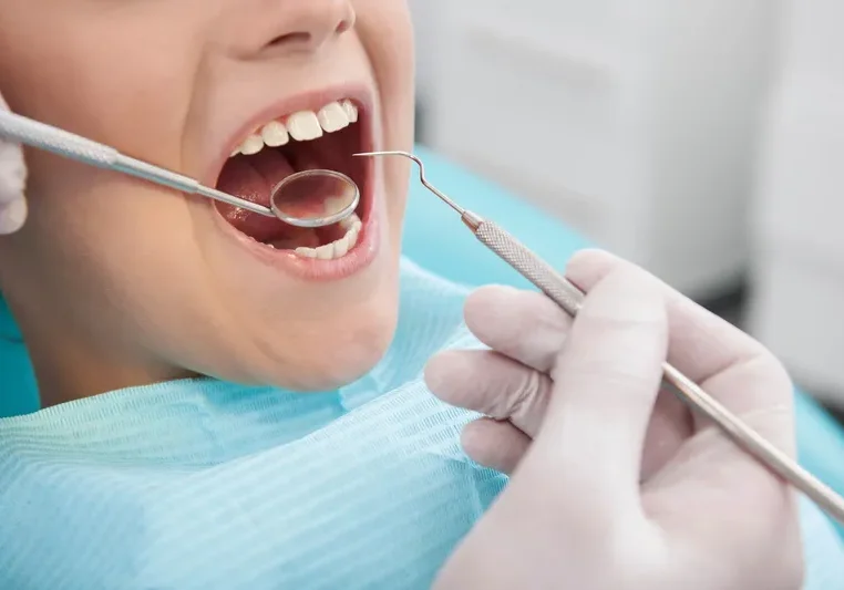 Woman getting her teeth examined by a dentist, with a person holding a dental tool in their hand