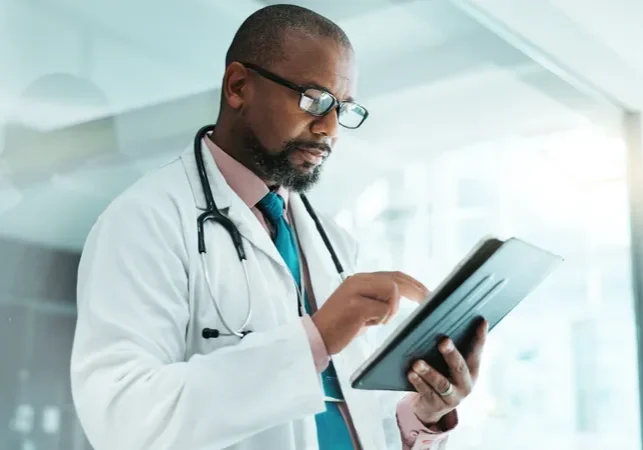 Male doctor wearing a coat and a stethoscope around his neck, holding a tablet computer in his hands