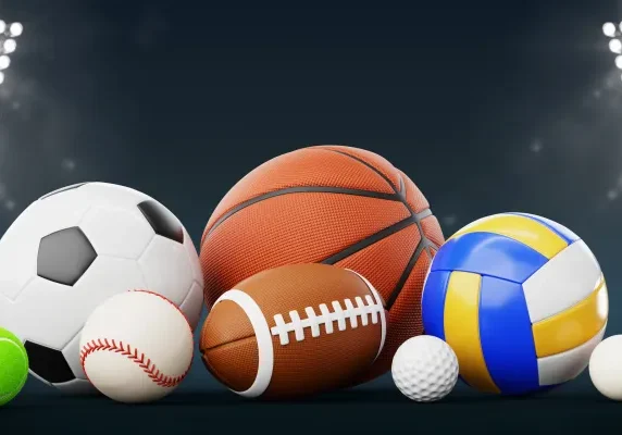 Group of different types of sports balls on a dark background, illuminated by flood lights