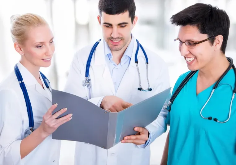 Three doctors wearing stethoscopes and looking at a clipboard, with a blurred background