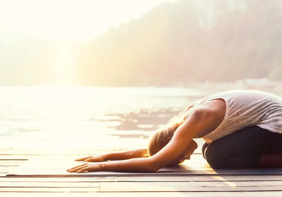 Woman in a yoga pose on a dock at sunset, with a wooden surface beneath her