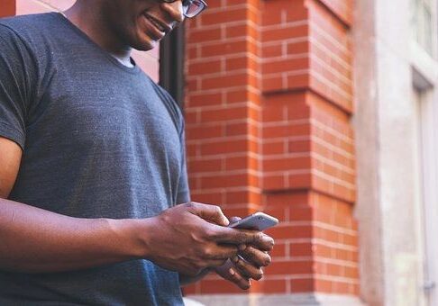 Man texting on smartphone near brick wall.