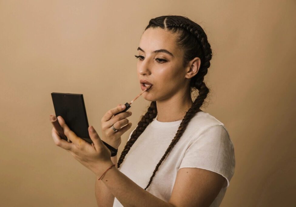 Woman applying lipstick, holding a mirror.